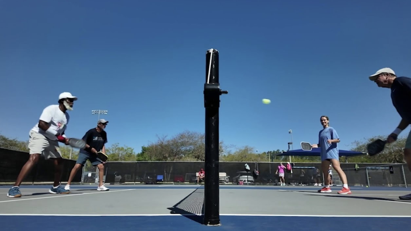 Doubles pickleball match on a blue court with permanent net at Veterans Park